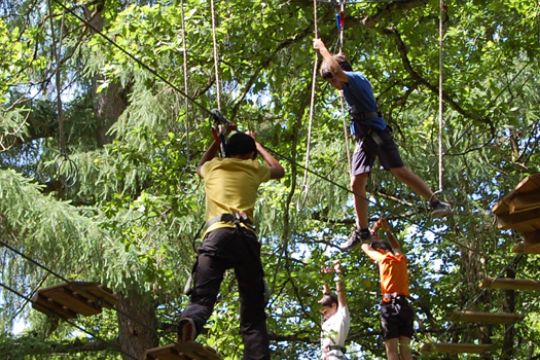 Cuatro niños con el equipamiento necesario para pasar por una cuerda rodeadas de árboles verdes en el parque de aventura de Hontzaextrem que está ubicado en Euskadi