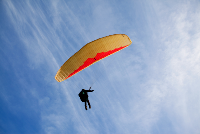  Fotografía que muestra cómo una persona vuela un parapente amarillo y rojo en un cielo despejado.