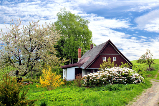 Una cabaña marrón y blanca rodeada de árboles y flores, un lugar ideal para dormir cerca del Parque Natural Cabárceno.
