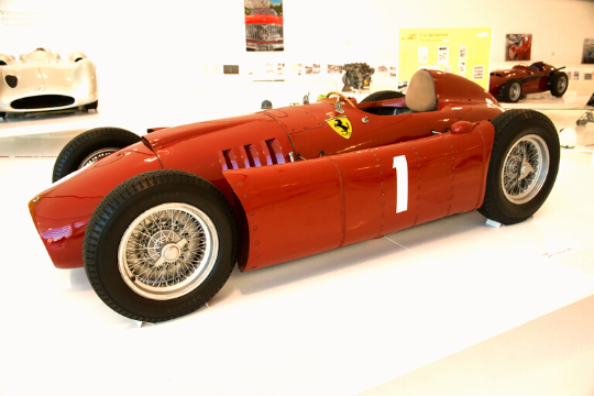 El Ferrari tipo 500 F2 de color rojo con el número 1 y ruedas negras está en un museo de coches.