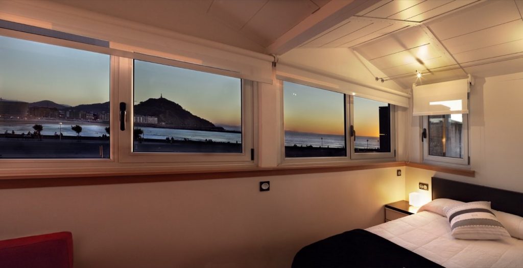 En la imagen se muestra una de las habitaciones del Hotel Punta Monpas de Donostia-San Sebastián, el cual tiene unas hermosas e increíbles vistas del anochecer de la ciudad, de la playa de Zurriola y del mar. 
